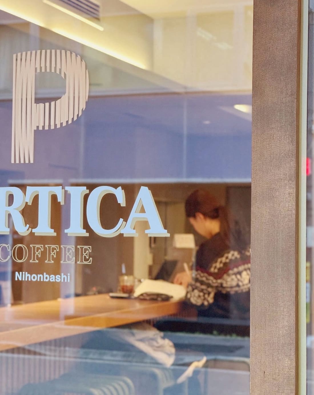 The PERTICA COFFEE Nihonbashi logo etched on the café window, a barista at work inside